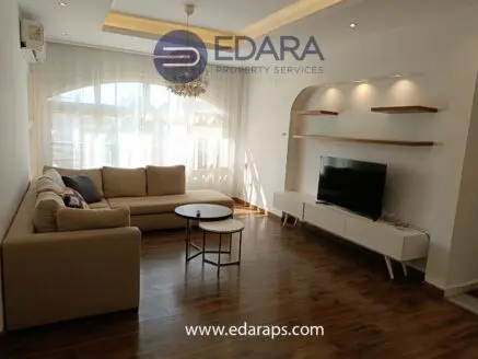 Contemporary living room featuring a beige sectional sofa, a coffee table, and a TV unit against a light-colored wall.