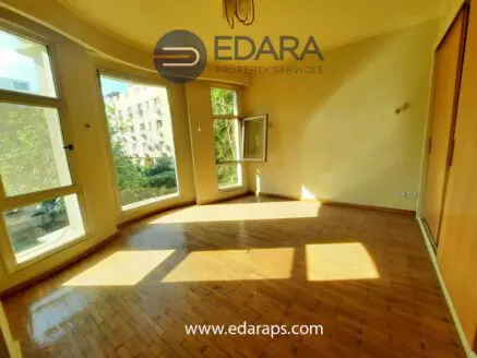 Bright empty room with large windows allowing natural light and wooden flooring.