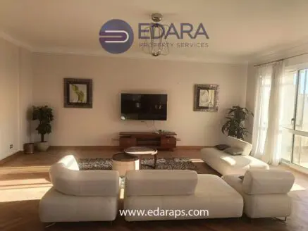 Spacious living room featuring a white sectional sofa and a television mounted on the wall.
