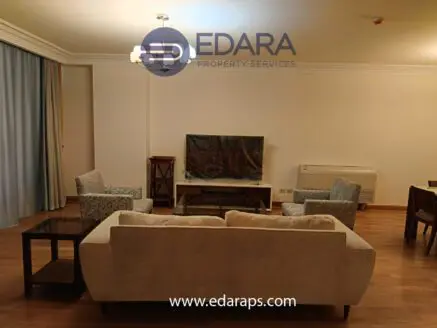 Living room featuring a beige sofa, two patterned chairs, and a television on a stand.