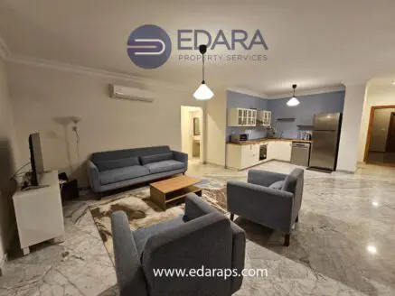Modern living room with gray sofas, coffee table, and kitchen area in an apartment setting.