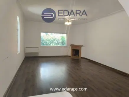 Interior view of a room featuring wooden flooring and a fireplace, with a window allowing natural light.