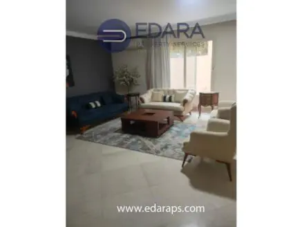 Living room featuring a blue sofa, white armchairs, and a wooden coffee table on a patterned rug.