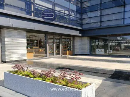 Entrance of a modern building featuring glass doors and a planter with greenery.