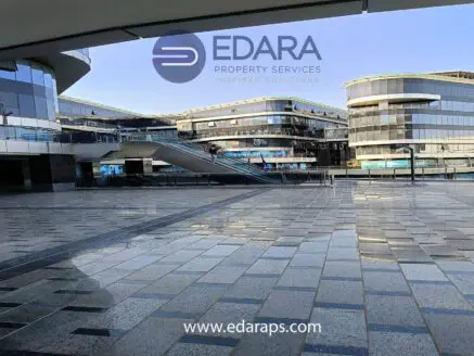 Exterior view of a modern commercial building with glass facades and a tiled plaza area.