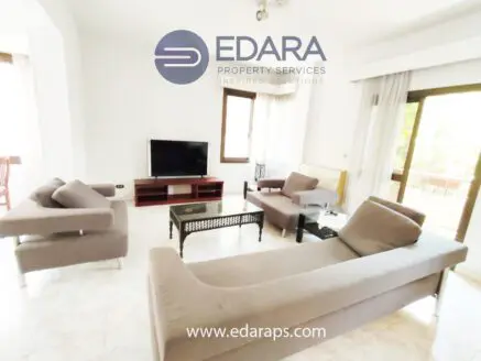 Spacious living room featuring a gray sofa set, coffee table, and television against a white wall.