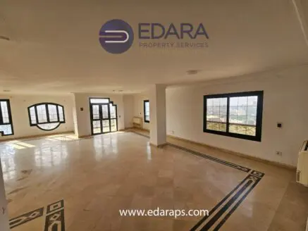 Interior view of a spacious room with large windows and marble flooring in a property.