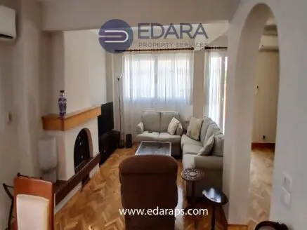 Spacious living room featuring a light-colored sofa, a fireplace, and large windows with curtains.
