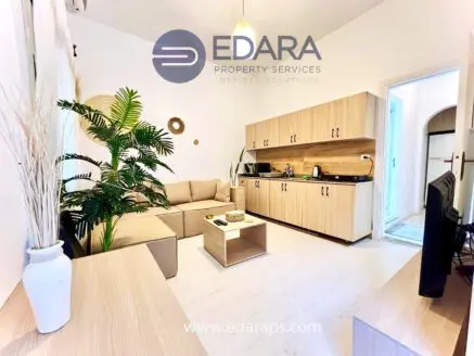 Contemporary living room featuring a beige sofa, wooden furniture, and a kitchenette area.