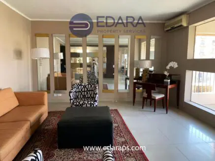 Contemporary living room featuring a brown sofa, patterned chair, and decorative table with a flower arrangement.