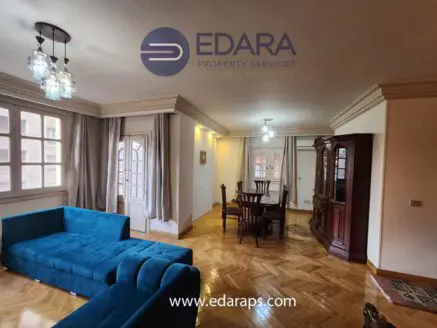 Interior view of a living room featuring a blue sofa and a wooden dining table with chairs.