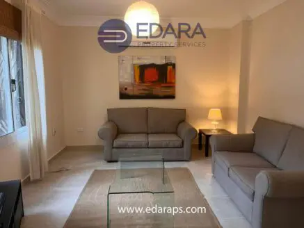 A living room featuring two beige sofas, a glass coffee table, and a lamp in a neutral-toned setting.