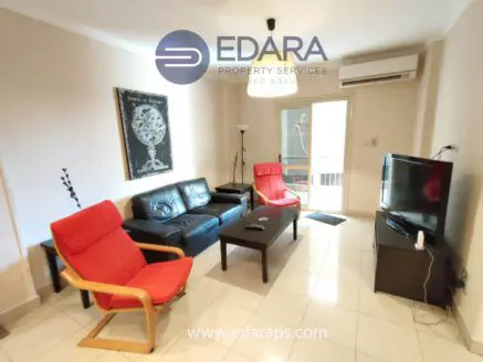 Living room featuring a black leather sofa, two red chairs, and a television on a stand.