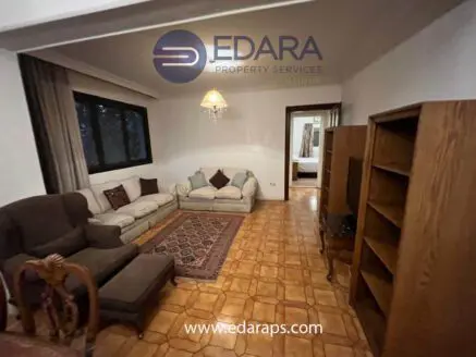 Living room featuring a beige sofa, wooden bookshelf, and decorative rug on tiled floor.