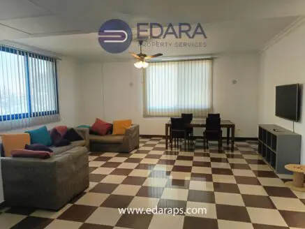 Living room featuring a sofa, colorful cushions, dining table, and television against a checkered floor.