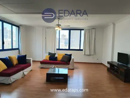 Living room featuring a sofa with colorful cushions and a coffee table in front of a large window.
