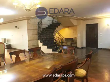 Dining area featuring a large wooden table and an ornate staircase in a residential interior.
