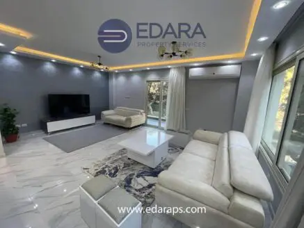 Spacious modern living room with light-colored furniture and a large TV on a white cabinet.