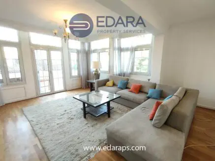 Spacious living room featuring a light gray sectional sofa with colorful cushions and a glass coffee table.