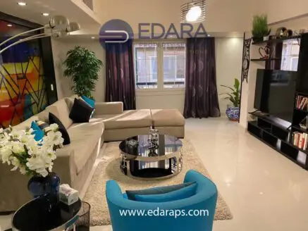 Contemporary living room featuring a beige sectional sofa, glass coffee table, and decorative plants.