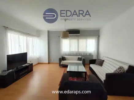 Bright living room featuring a sofa, coffee table, and television against a wall of windows.