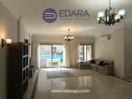 Spacious living room featuring a gray sofa, coffee table, and large windows overlooking a pool area.