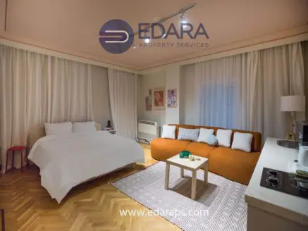 Interior view of a modern living room featuring a bed and an orange sofa with decorative pillows.