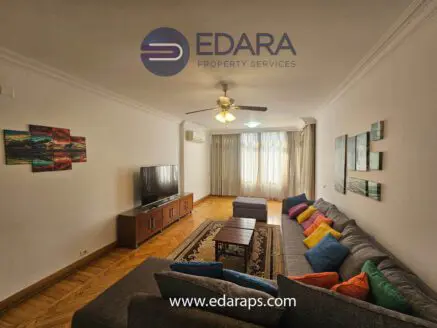 Spacious living room featuring a gray sofa, wooden coffee table, and a television against a light-colored wall.