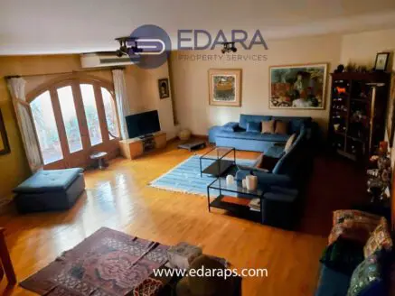 Spacious living room featuring a large blue sofa, wooden flooring, and a television unit.