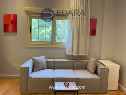 Contemporary gray sofa with two cushions in a well-lit indoor setting with a window.