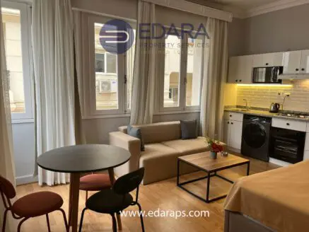 Interior view of a modern apartment featuring a living area with a sofa, dining table, and kitchen appliances.