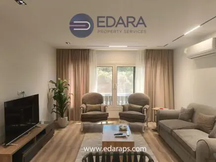 Modern living room featuring a sofa, armchairs, television, and large windows with curtains.