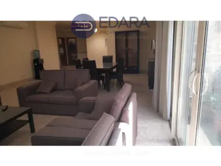 Interior view of a living room featuring gray sofas and a dining area in the background.
