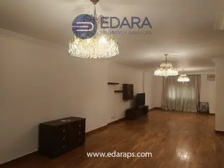 Bright living room featuring two elegant chandeliers and wooden flooring, with a television and furniture.