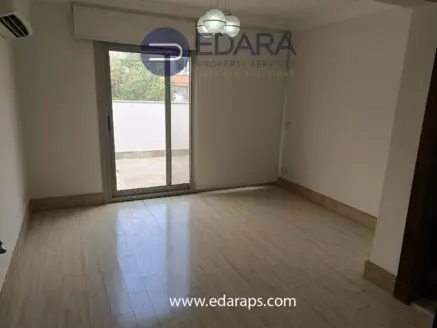 Interior view of an empty room featuring a large window and wooden flooring.