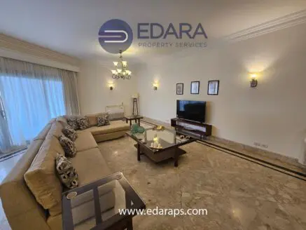 Spacious living room featuring a large beige sofa, coffee table, and television on a wooden stand.