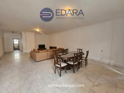 Interior view of a spacious living room featuring a dining table and seating area with marble flooring.