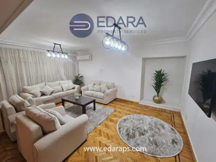 Modern living room featuring a light-colored sofa set, decorative plant, and a contemporary light fixture.