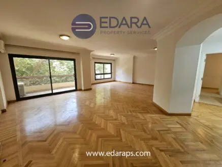 Interior view of a spacious room featuring parquet flooring and large windows allowing natural light.
