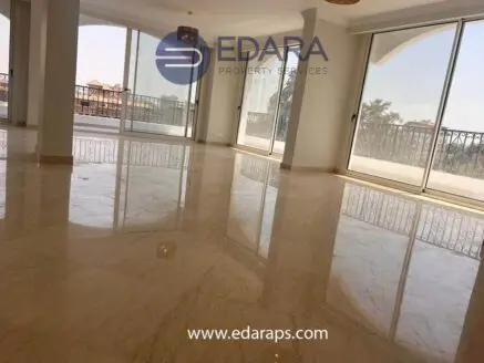 Interior view of a spacious room with marble flooring and large glass windows allowing natural light.