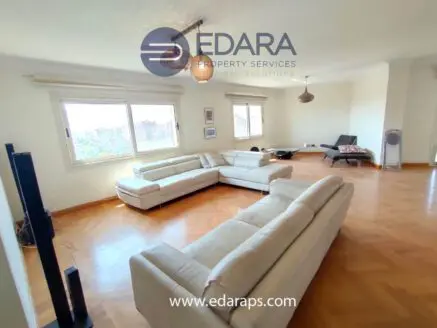 Bright living room featuring a light-colored sectional sofa and large windows providing natural light.