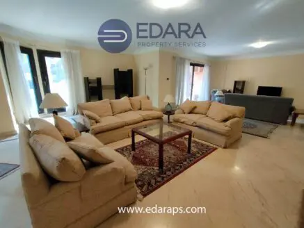 Living room featuring a large beige sofa set arranged around a glass coffee table on a patterned rug.