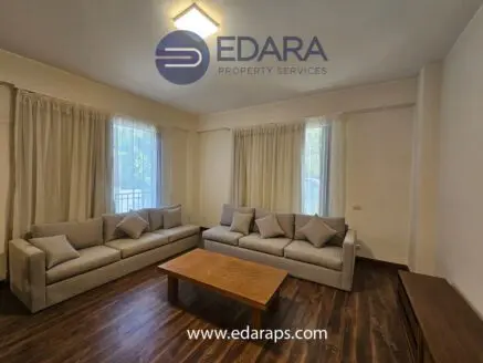 Spacious living room featuring two light gray sofas and a wooden coffee table under natural light from windows.