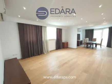 Bright living room featuring wooden flooring, large windows, and curtains in neutral tones.