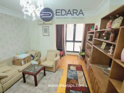 Living room featuring beige sofas, a glass coffee table, and wooden shelving with decorative items.