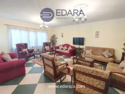 Living room featuring a red sofa, patterned armchairs, and a television on a stand.