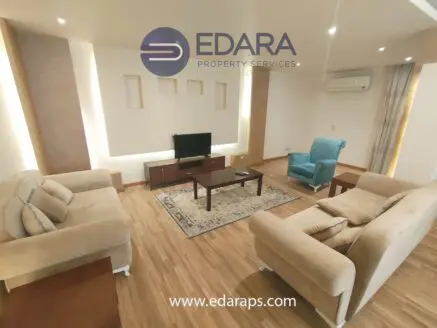 Modern living room featuring a beige sofa set, coffee table, and television in a well-lit space.