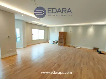 Spacious empty room with wooden flooring and natural light from large windows.