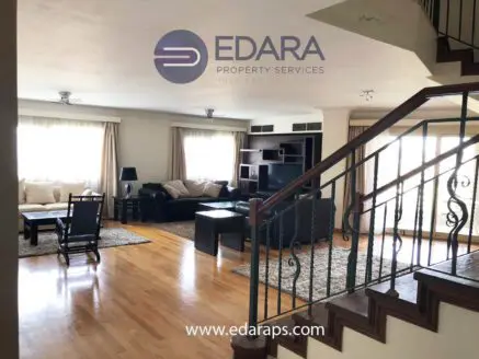 Bright living room featuring a sofa set, coffee table, and wooden staircase with railing.