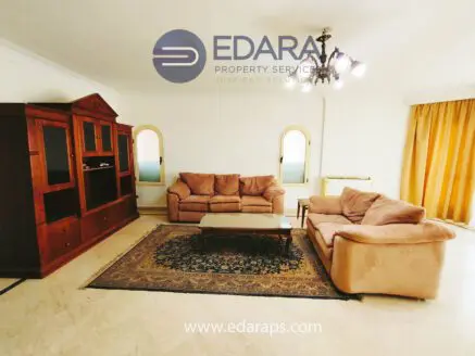 Living room featuring beige sofas, a wooden cabinet, and a decorative rug on the floor.